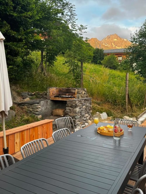 Outdoor dining terrace at Chalet école des Cîmes with mountain views, stone fireplace, and wooden deck