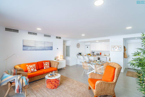 Moderno salón diáfano de loft con sofá naranja, sillas de mimbre, cocina y obra de arte con vista al mar en Alhaurín