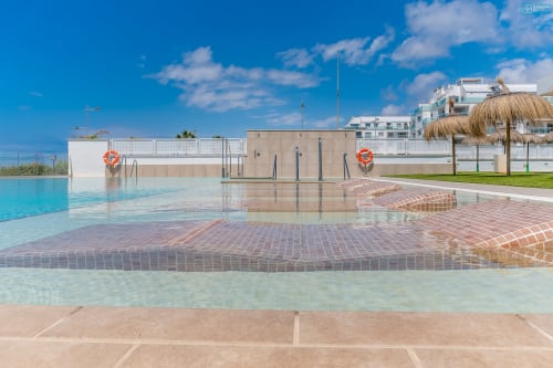 Piscina de lujo frente al mar en Alhaurín Loft City Center con agua turquesa cristalina, patio de ladrillo y apartamentos modernos bajo cielo azul