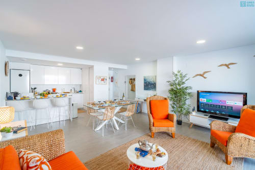 Apartamento moderno de planta abierta con cocina blanca, sillas naranjas, mesa comedor y TV en Alhaurín de la Torre