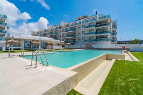 Piscina turquesa con tumbonas y sombrillas de paja en el complejo de apartamentos de lujo Alhaurín Loft City Center