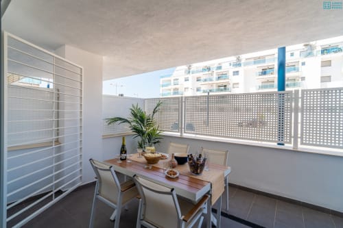 Moderno balcón terraza en Alhaurín Loft con mesa de comedor, sillas, planta en maceta y paneles perforados de privacidad