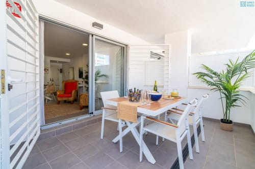 Terraza de comedor al aire libre con mesa de madera, sillas blancas y vistas al mar en Maruchis Beachfront Luxury Apartment en Alhaurín de