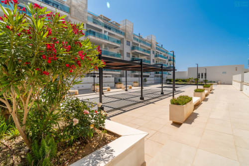 Terraza moderna en la azotea del Alhaurín Loft con flores rojas, áreas de descanso, pérgola y vistas a la ciudad bajo cielo azul