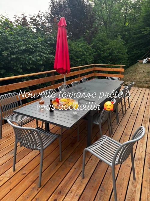 New terrace at Chalet école des Cîmes with dining table, chairs, red umbrella and forest view