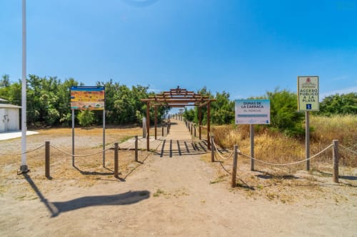 Sendero de acceso a la playa con pérgola de madera y vegetación dunar en las Dunas de la Carraca, Alhaurín de la Torre, España