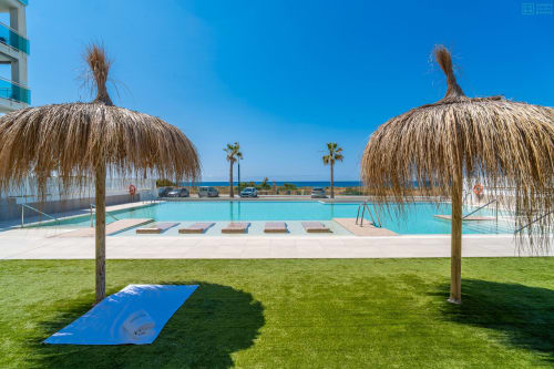 Piscina de lujo frente al mar con palapas de paja, tumbonas y vistas al mar en el complejo Alhaurín Loft