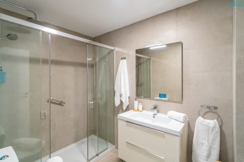 Baño moderno en apartamento de lujo de Alhaurín con ducha de cristal, tocador blanco, espejo y acabados en azulejos beige