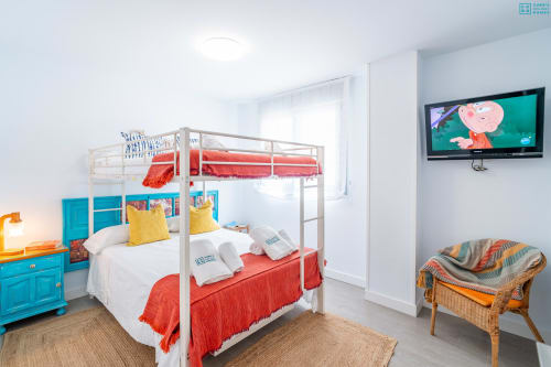 Dormitorio infantil colorido con camas literas, mesita de noche turquesa, televisión y vistas al mar