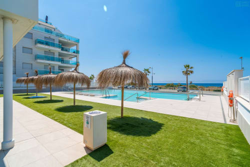 Piscina y terraza frente al mar en Alhaurín Loft con agua turquesa, sombrillas de paja y vistas al Mediterráneo.