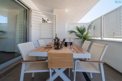Moderna zona de comedor al aire libre en la terraza de Alhaurín Loft con muebles blancos, mesa de madera y vistas de la ciudad