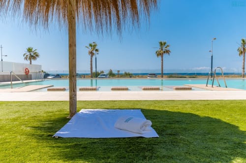 Piscina frente al mar en Alhaurín Loft con agua turquesa, palmeras, vista al mar y toallas en el césped