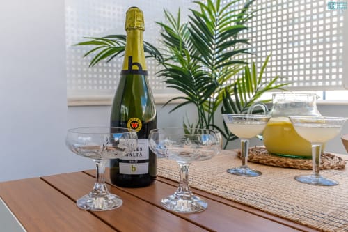 Botella de champagne con copas sobre mesa de madera en el apartamento Alhaurín Loft con plantas y vistas al mar desde el balcón
