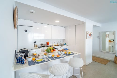 Cocina moderna y zona de comedor en apartamento de lujo en Alhaurín con muebles blancos, barra de desayuno y frutas frescas