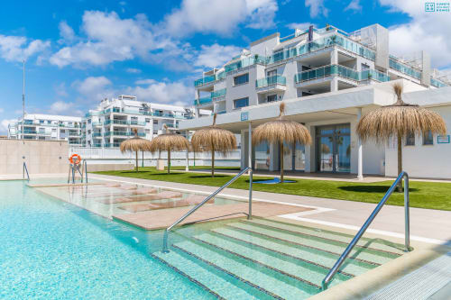 Piscina de complejo de lujo moderno con sombrillas de paja, agua turquesa y edificios blancos en Alhaurín de la Torre