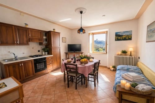 Spacious cottage apartment with wood kitchen, dining area with red checkered tablecloth, bed, and Tuscan countryside landmark