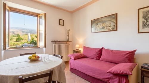 Cozy cottage room at I Castagnini with pink sofa, countryside view, and Tuscan landscape from window