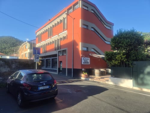 Hotel Sereno a Sestri Levante con facciata rosso-arancio, auto parcheggiata, vista sulle montagne e ingresso stradale