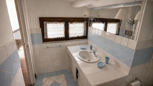 Luminoso bagno di B&B a Palermo con lavabo bianco, bidet, pareti piastrellate, finestre con tendine di pizzo e specchio.