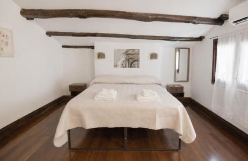 Ampia camera da letto presso Politeama Central Suite a Palermo con travi in legno a vista, letto matrimoniale, pavimenti in legno massello e vista montagne