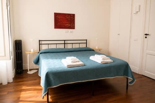 Camera moderna della Politeama Central Suite a Palermo con coperta turchese, letto in metallo nero, pavimenti in legno e accenti rossi