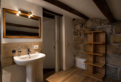 Bagno moderno nella Politeama Central Suite di Palermo con lavabo su piedistallo, specchio, mensole in legno e muri in pietra a vista