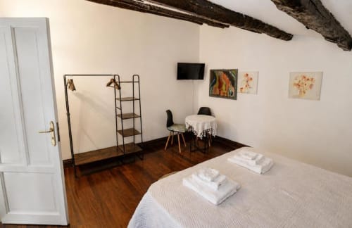 Spaziosa camera da letto nella Politeama Central Suite di Palermo con pavimenti in legno, travi a vista, biancheria bianca, TV e tavolo da pranzo