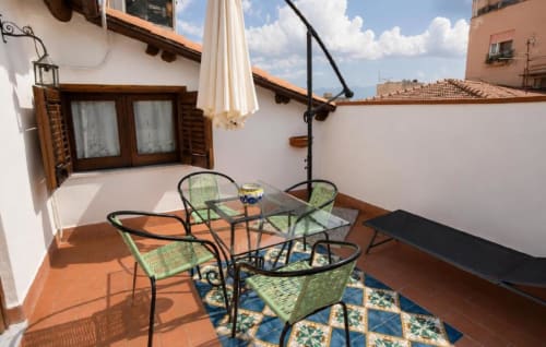 Terrazza soleggiata della Politeama Central Suite a Palermo con sedie verdi, tavolo in vetro e ombrellone con vista sulla città