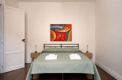 Camera moderna al Politeama Central Suite Palermo con copriletto verde, letto in metallo nero, comodini in legno e dettagli colorati