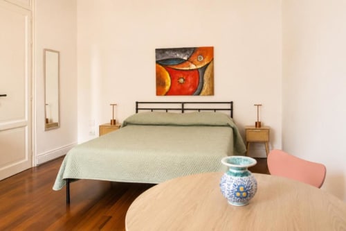 Camera da letto moderna e luminosa presso Politeama Central Suite Palermo con biancheria verde, tavolo in legno con vaso di ceramica e dettagli colorati