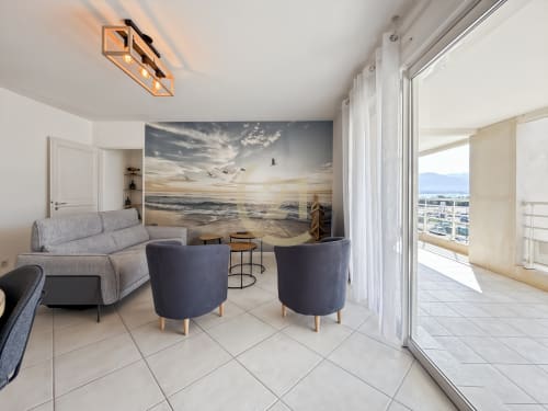 Séjour moderne à Calvi avec vue sur mer, mobilier gris, fresque plage et accès terrasse