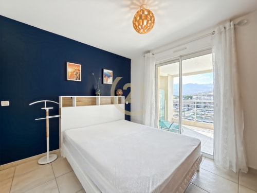 Chambre moderne avec mur d'accent bleu marine, lit blanc et balcon avec vue sur la mer à Calvi, Corse