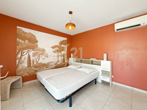 Chambre orangée lumineuse avec lit blanc et fresque méditerranéenne dans un appartement à Calvi avec vue mer