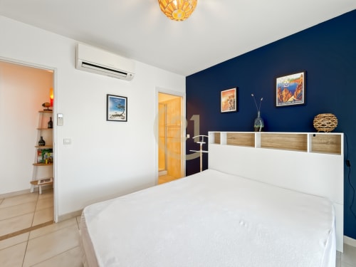 Chambre moderne de l'appartement de Calvi avec lit blanc, mur d'accent bleu marine, mobilier en bois et décoration vue mer