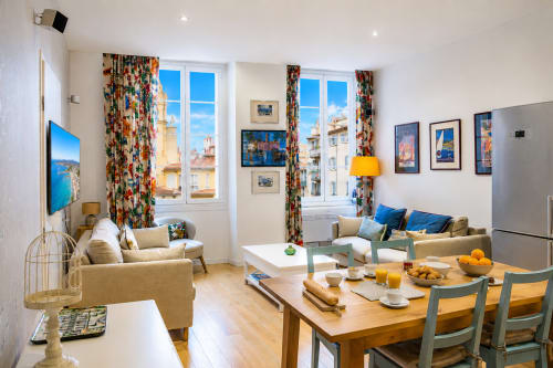 Bright modern apartment in Nice with colorful curtains, furnished living area, dining table, and blue sea views from windows