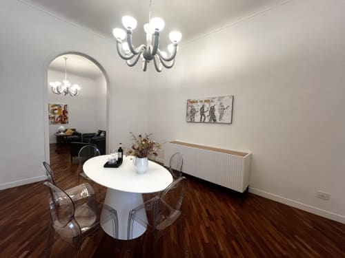 Zona living moderna in appartamento Bari con tavolo rotondo bianco, sedie trasparenti, lampadario e pavimenti in legno