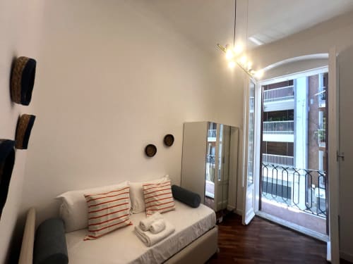 Camera moderna agli Appartamenti Bari con divano bianco, cuscini a righe rosse, balcone vista città e illuminazione contemporanea