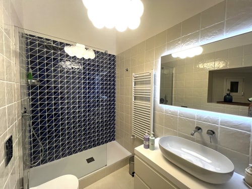 Bagno moderno in Appartamenti Bari con doccia in piastrelle geometriche nere, lavabo bianco, specchio illuminato e asciugamani