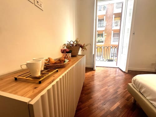Accogliente camera negli Appartamenti Bari con scrivania in legno, tazza bianca, cesto, pavimenti in parquet e vista città dal balcone