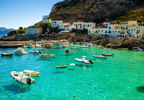 Caletta turchese del Mediterraneo con barche ormeggiate e edifici imbiancati a calce nel villaggio di Villa Giulia sul Mare, spiaggia di Marausa
