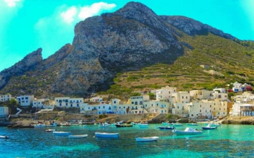 Villaggio costiero colorato con barche in acque turchesi, montagne rocciose, Villa Giulia sul Mare, lido di Marausa Sicilia