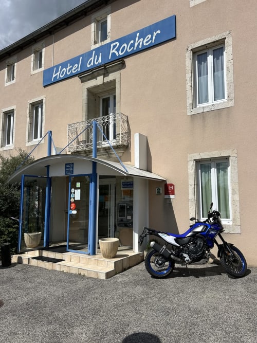 Entrée de l'Hôtel du Rocher au Caylar avec façade moderne bleue et blanche, moto bleue et noire garée devant