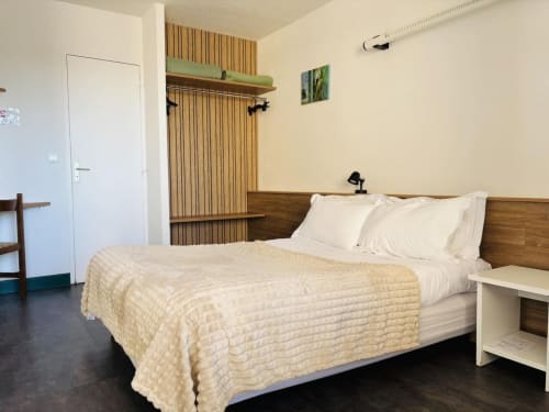 Chambre moderne de l'Hôtel Du Rocher au Caylar avec lit en bois, literie crème et décoration minimaliste