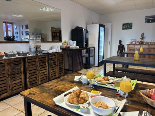 Hotel Du Rocher breakfast room in Le Caylar with wooden tables, pastries, juice, and coffee service