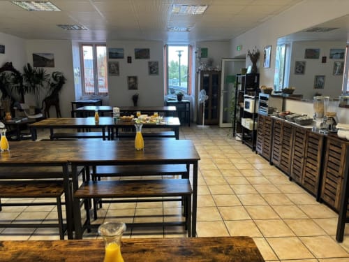 Spacieuse salle de petit-déjeuner de l'Hôtel Du Rocher au Caylar avec tables en bois, bancs, plantes et fenêtres ensoleillées