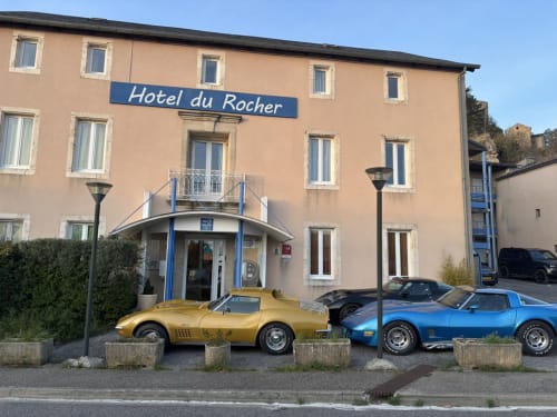 Entrée de l'Hôtel du Rocher avec voitures de sport vintage à Le Caylar, France