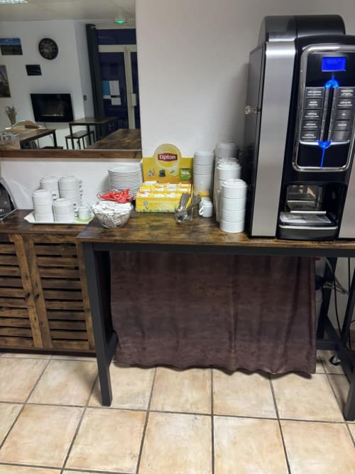 Station café de l'Hôtel Du Rocher avec présentoir de thé Lipton, tasses et distributeur de boissons moderne au Caylar