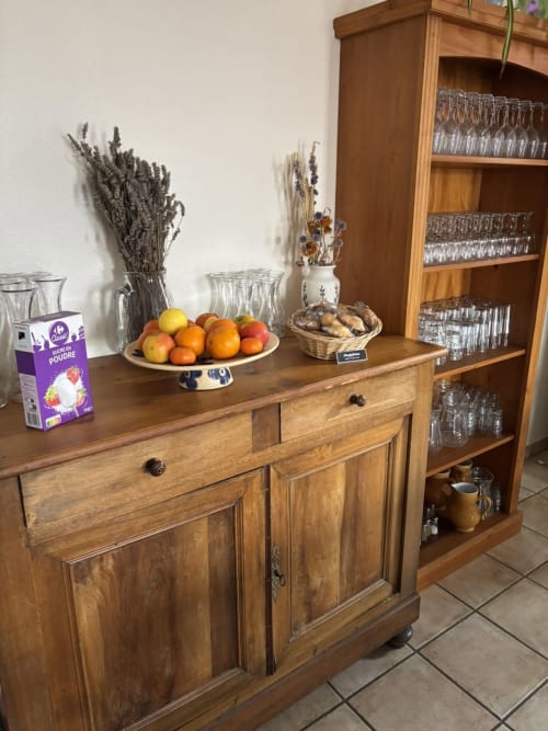 Wooden sideboard with fresh fruit display, dried flowers, and glasses at Hôtel Du Rocher in Le Caylar