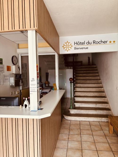 Hôtel du Rocher reception desk with welcome sign and wooden stairs in Le Caylar