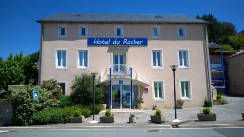 Hôtel du Rocher in Le Caylar, France - peachy facade with blue signage and entrance courtyard